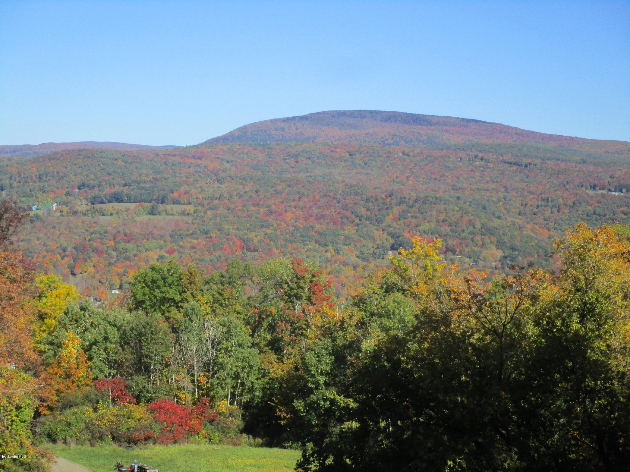 The bald summit dome of Mount Greylock rising above a brilliant sea of red and orange autumn foliage seen from High Meadows Farm